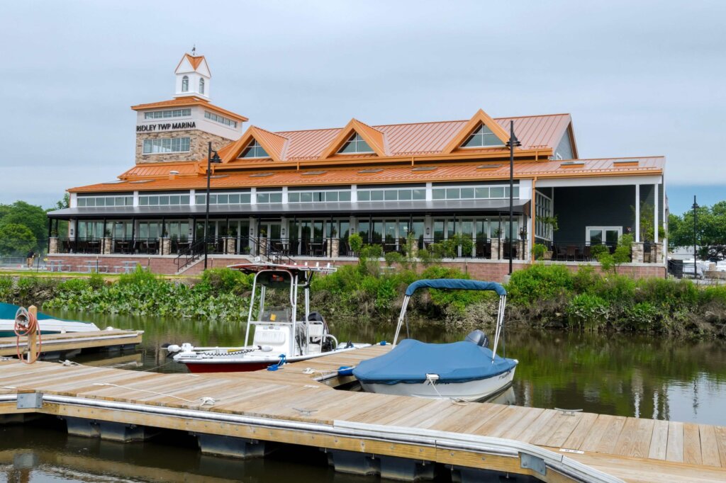 Edificio de la marina de Holly TWP con un distintivo tejado naranja y grandes ventanales, situado junto a un muelle con embarcaciones.