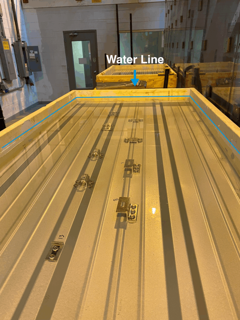 Línea de agua visible en una mesa grande, con soportes S-5! instalados en una muestra de material de techo de metal sumergido en agua.