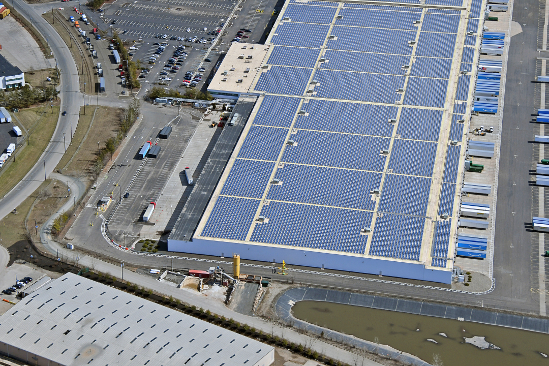 Aerial view of a large industrial warehouse with an expansive solar panel array covering its flat roof.