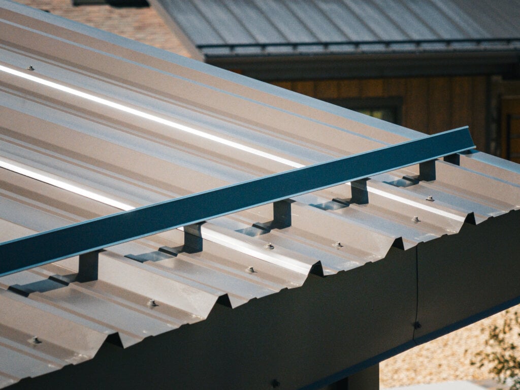 Grey corrugated metal roof with a thin blue horizontal rail mounted on small grey supports.